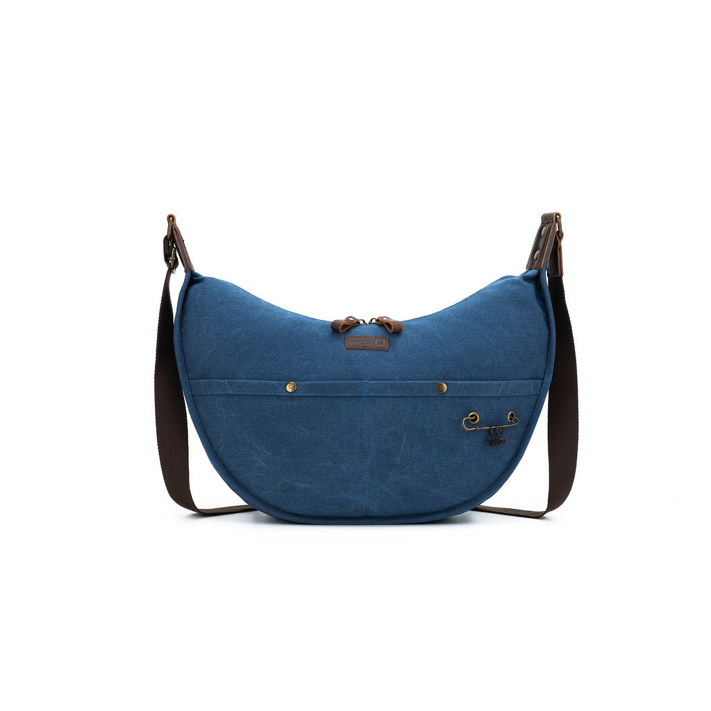 Crescent project bag in deep indigo blue with brown strap and leather accents. Features della Q logo patch, front pockets, yarn guide, and antique brass hardware.